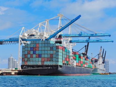 Cargo ship at Miami harbor with crane and blue sky over sea.